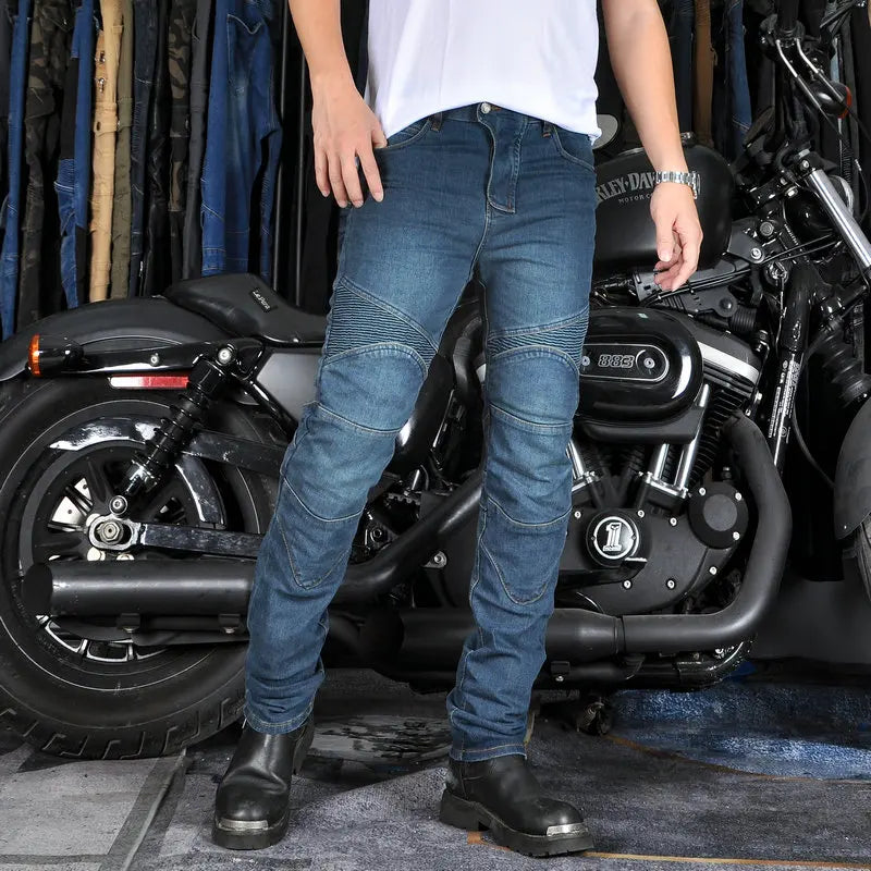 Person wearing blue jeans and black shoes standing in front of a motorcycle.