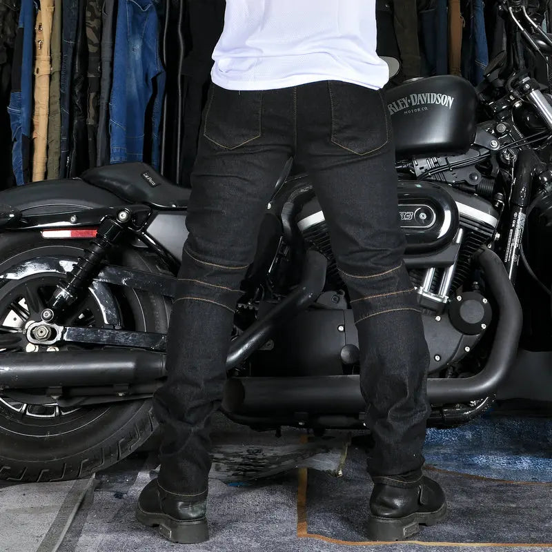 Person wearing black jeans and boots standing next to a Harley Davidson motorcycle in a garage.