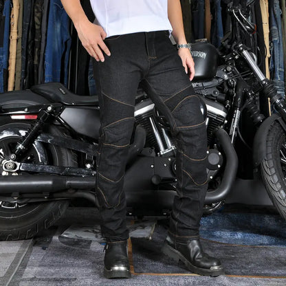 Person wearing black motorcycle pants and boots standing next to a motorcycle in a garage.